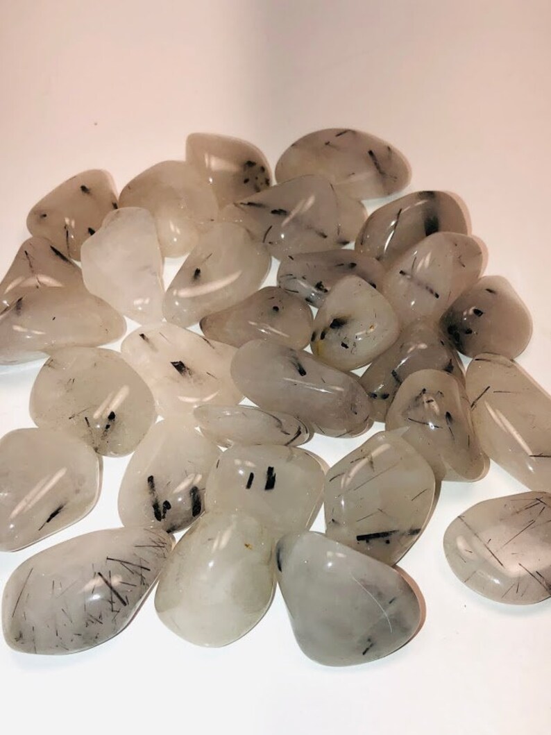Puede incluir: Una colecci&oacute;n de piedras de cuarzo transparente pulidas con inclusiones de turmalina negra. Las piedras son lisas y pulidas, con una variedad de formas y tama&ntilde;os.
