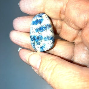 May include: A smooth, oval-shaped blue and white kyanite gemstone. The stone has a swirling pattern of blue and white.