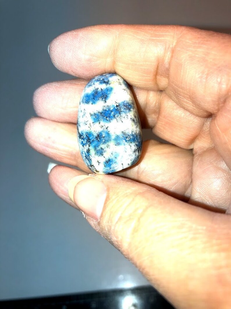 May include: A smooth, oval-shaped blue and white kyanite gemstone. The stone has a swirling pattern of blue and white.