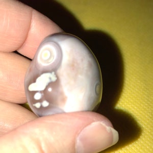 May include: A smooth, white agate stone with brown and white markings. The stone has a circular pattern on one side.