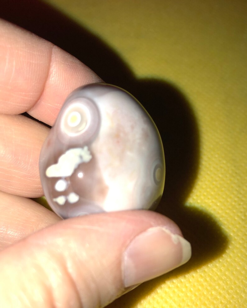 May include: A smooth, white agate stone with brown and white markings. The stone has a circular pattern on one side.