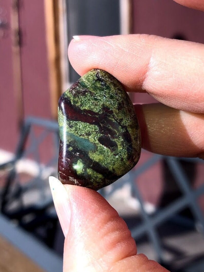 May include: A green and red polished stone with swirling patterns. The stone is smooth and has a natural, organic look.