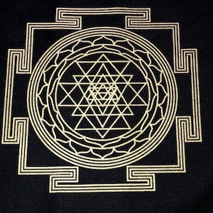 May include: Black textile featuring a gold-colored Sri Yantra design. The geometric pattern includes interlocking triangles, circles, and a square border. The design is centered and symmetrical, creating a visually balanced composition.