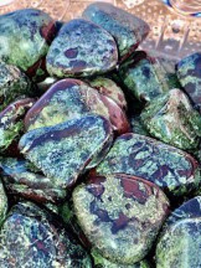 May include: A collection of tumbled green and red jasper stones with a mottled pattern. The stones are smooth and polished.