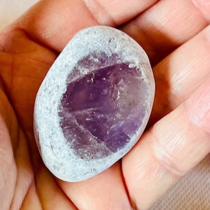 May include: A smooth, white and purple amethyst stone with a natural, rounded shape.