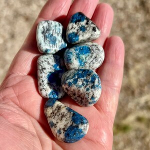 May include: A collection of five blue and white tumbled stones. The stones are smooth and have a speckled pattern.
