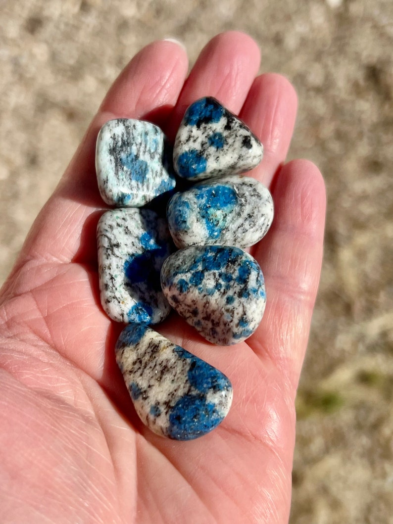 May include: A collection of five blue and white tumbled stones. The stones are smooth and have a speckled pattern.