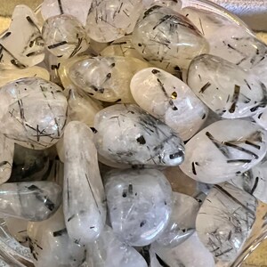 Puede incluir: Una colecci&oacute;n de piedras de turmalina negra y cuarzo transparente pulidas. Las piedras son lisas y pulidas, con una variedad de formas y tama&ntilde;os. La turmalina negra es una piedra oscura y opaca, mientras que el cuarzo transparente es transparente y brillante.