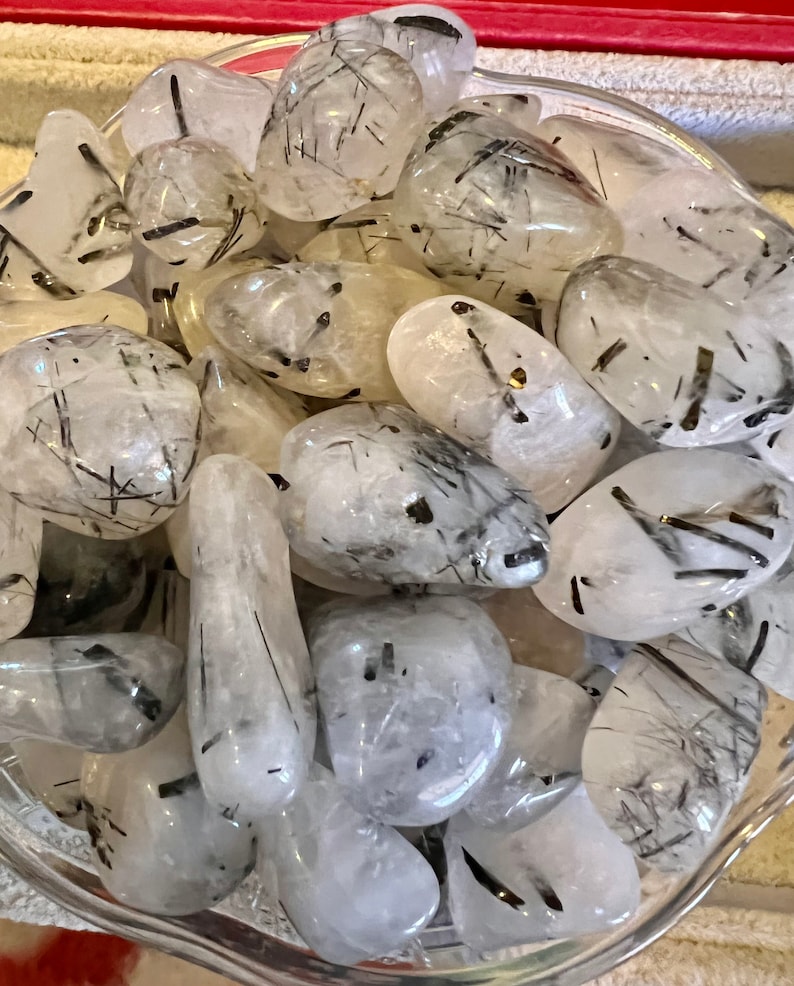 Puede incluir: Una colecci&oacute;n de piedras de turmalina negra y cuarzo transparente pulidas. Las piedras son lisas y pulidas, con una variedad de formas y tama&ntilde;os. La turmalina negra es una piedra oscura y opaca, mientras que el cuarzo transparente es transparente y brillante.