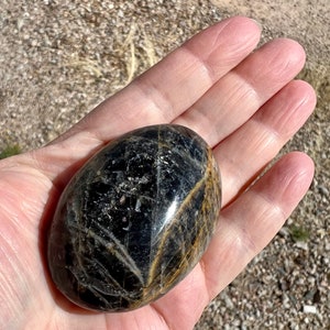 May include: A smooth, oval-shaped black gemstone with gold streaks and a high gloss finish.