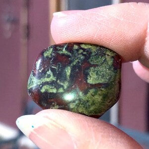 May include: A green and red jasper stone with a smooth, polished surface. The stone has a unique pattern of green and red swirls.