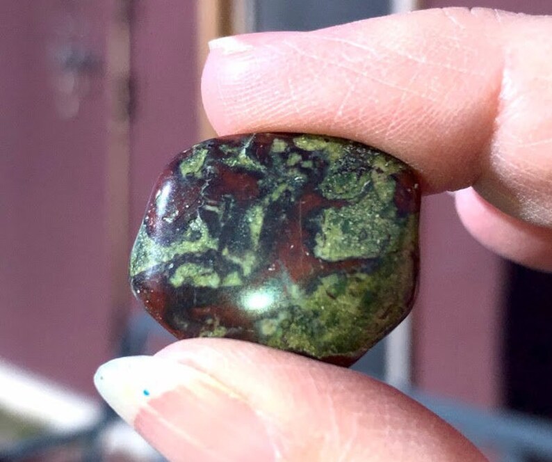May include: A green and red jasper stone with a smooth, polished surface. The stone has a unique pattern of green and red swirls.