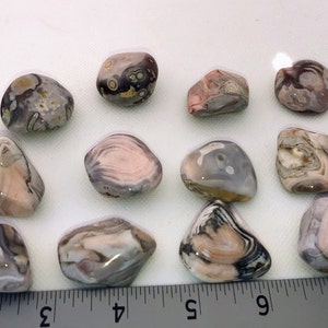 May include: A collection of 15 tumbled agate stones in various shades of pink, brown, and gray with intricate patterns. The stones are smooth and polished, with a natural, organic look.