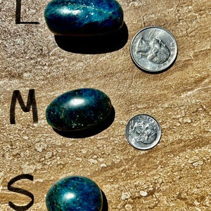 Puede incluir: Tres piedras pulidas de color azul verdoso de diferentes tama&ntilde;os, etiquetadas como "L", "M" y "S" para grande, mediano y peque&ntilde;o. Cada piedra est&aacute; junto a una moneda de 25 centavos de d&oacute;lar estadounidense para comparar el tama&ntilde;o.