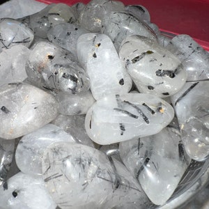 Puede incluir: Un cuenco lleno de piedras de cuarzo transparente pulidas con inclusiones de turmalina negra. Las piedras son lisas y pulidas, con una variedad de formas y tama&ntilde;os.
