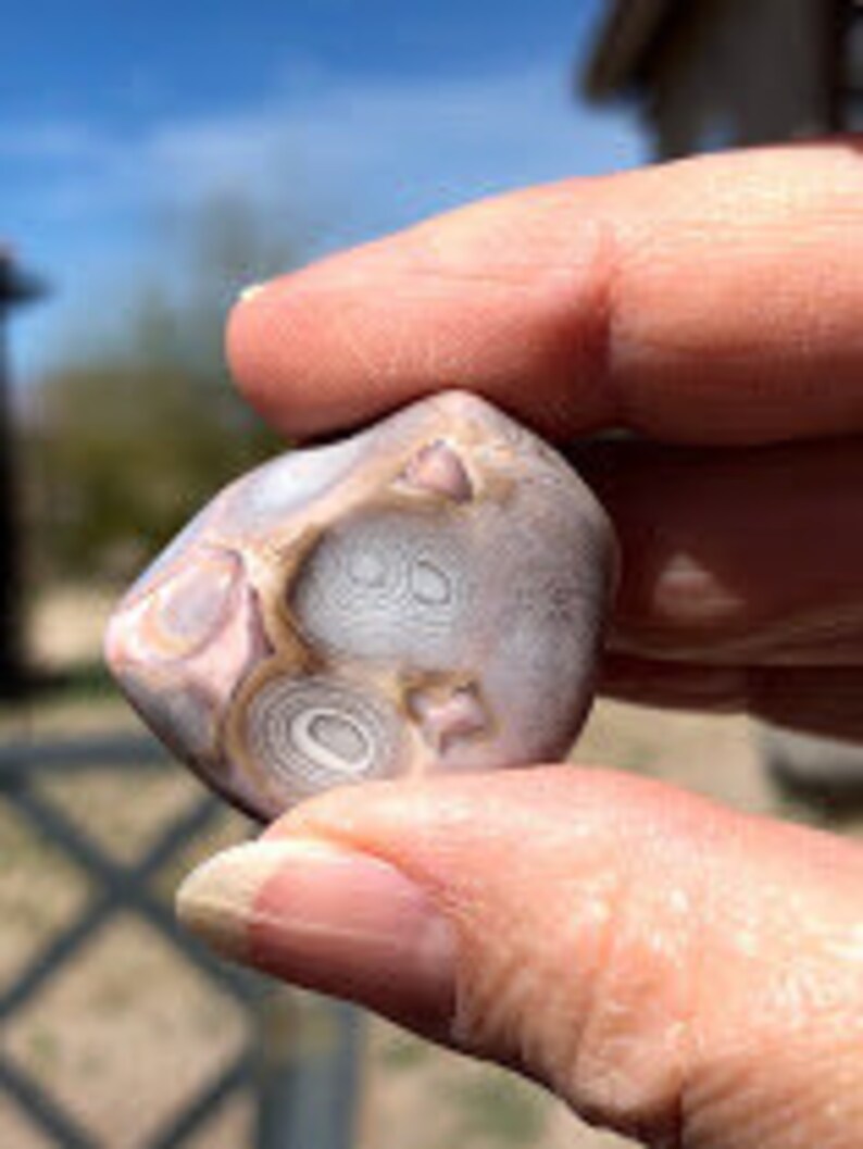 May include: A close-up of a small, irregularly shaped agate stone with a swirling pattern of white, brown, and gray. The stone has a smooth, polished surface.