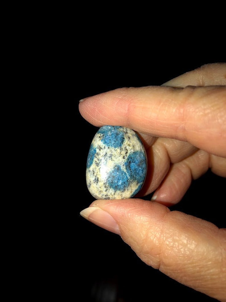 May include: A smooth, polished blue and white stone with a speckled pattern. The stone is oval shaped and has a glossy finish.