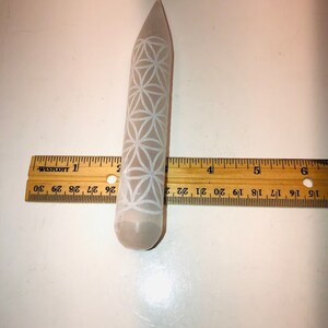May include: A white selenite wand with a carved flower of life design. The wand is approximately 4 inches long and is measured against a ruler.