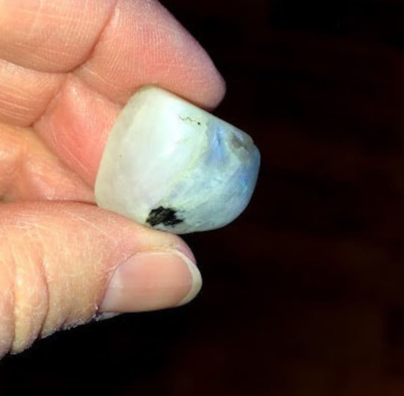 May include: A smooth, white moonstone with a blue iridescent sheen. The stone is irregularly shaped and has a few black inclusions.