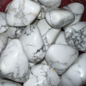 May include: A collection of white howlite tumbled stones with gray veining. The stones are smooth and polished, and they are arranged in a bowl.