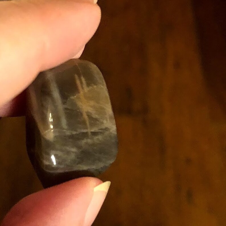 May include: A smooth, gray and white gemstone with a unique pattern. The stone is tumbled and has a polished finish.