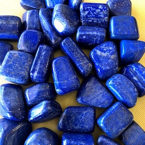 May include: A collection of tumbled lapis lazuli stones. The stones are a deep blue color with white veins running through them. The stones are smooth and polished.