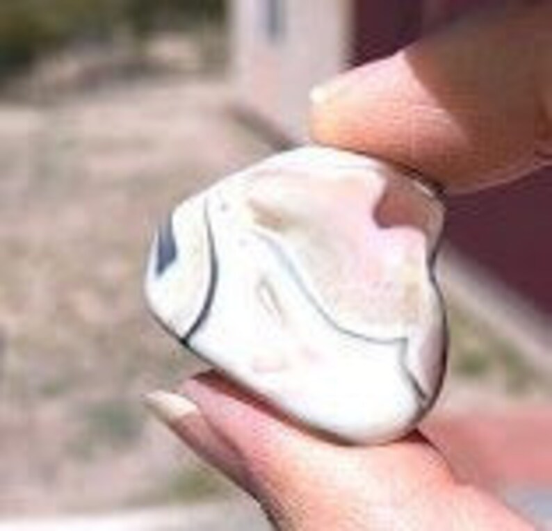 May include: A white agate stone with black and gray banding. The stone is smooth and polished, with a heart-shaped outline.