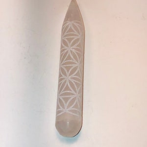 May include: A white selenite wand with a carved flower of life design. The wand is smooth and polished.