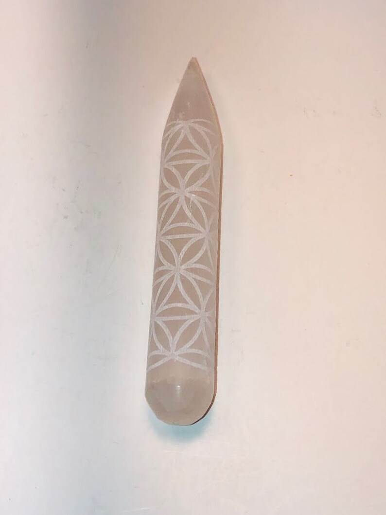 May include: A white selenite wand with a carved flower of life design. The wand is smooth and polished.