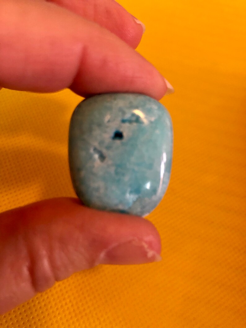 May include: A smooth, light blue, oval-shaped gemstone with white marbling. The stone has a few small, dark spots.