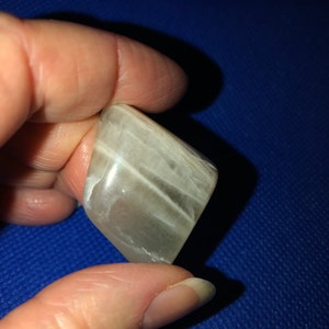 May include: A white, translucent, smooth, rectangular stone with white streaks. The stone is being held by a hand.
