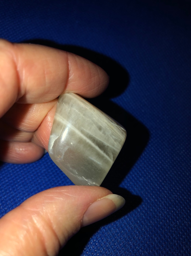 May include: A white, translucent, smooth, rectangular stone with white streaks. The stone is being held by a hand.