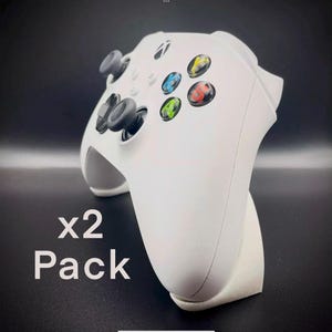 May include: A white Xbox controller with black buttons and a white stand. The text "x2 Pack" is visible in the image.
