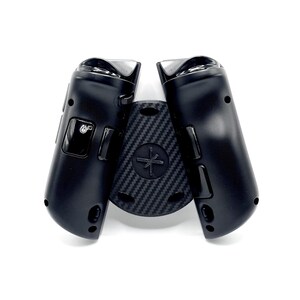 May include: Black gaming controller with a carbon fiber textured center piece. The controller has a sleek design with buttons and a joystick. The center piece features a cross-shaped design. The controller is designed for gaming.