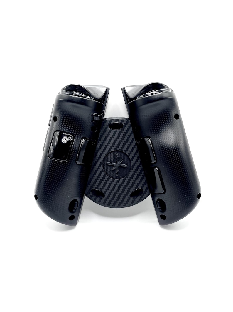 May include: Black gaming controller with a carbon fiber textured center piece. The controller has a sleek design with buttons and a joystick. The center piece features a cross-shaped design. The controller is designed for gaming.