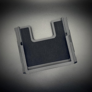 Puede incluir: Una funda de tel&eacute;fono rectangular gris con un recorte en forma de U y un interior gris oscuro. La funda tiene una superficie texturizada y un dise&ntilde;o minimalista, adecuada para proteger un tel&eacute;fono inteligente.