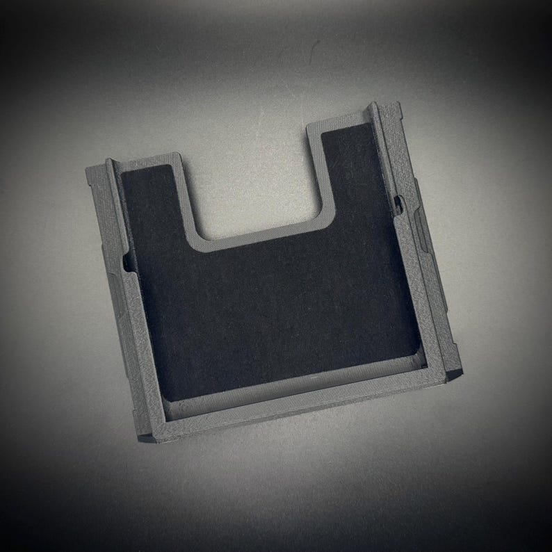 Puede incluir: Una funda de tel&eacute;fono rectangular gris con un recorte en forma de U y un interior gris oscuro. La funda tiene una superficie texturizada y un dise&ntilde;o minimalista, adecuada para proteger un tel&eacute;fono inteligente.