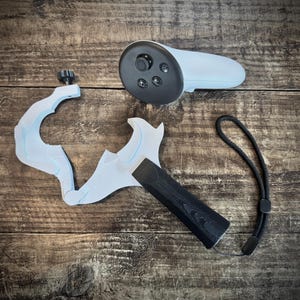 May include: A disassembled VR controller setup, featuring a light blue controller, a white grip, and a black handle. A black wrist strap is also included. The components are arranged on a wooden surface.