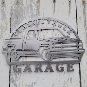 May include: Metal sign with a silhouette of a classic truck and the words "Classic Truck Garage".