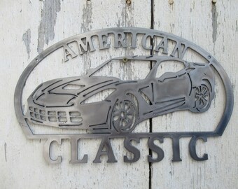 Könnte beinhalten: Metallwandkunst mit einer Silhouette eines Corvette mit den Worten "AMERICAN CLASSIC" in einem geschwungenen Banner über dem Auto.