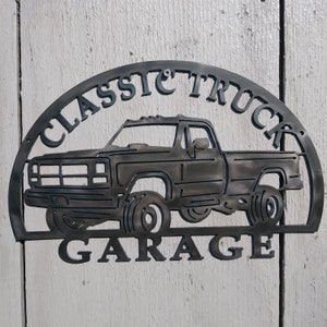 Pode incluir: Um sinal de metal preto com a silhueta de um caminhão clássico e o texto "CLASSIC TRUCK GARAGE".