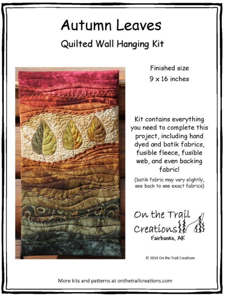 May include: A quilted wall hanging kit featuring autumn leaves in shades of red, orange, yellow, and green. The kit includes hand-dyed and batik fabrics, fusible fleece, fusible web, and backing fabric. The finished size is 9 x 16 inches.  "On the Trail Creations" is printed on the bottom right corner of the image.