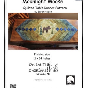 May include: Quilted table runner pattern featuring a moose silhouette in a forest scene. The pattern is called "Moonlight Moose" and is by Beret Nelson. The finished size is 11 x 34 inches. The pattern is available from On the Trail Creations in Fairbanks, Alaska.