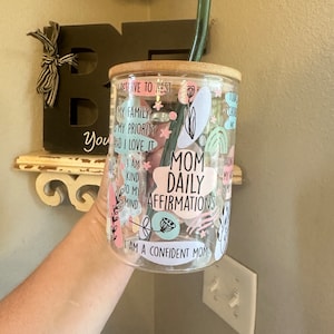 May include: A clear glass tumbler with a bamboo lid and a pink, blue, and green design. The tumbler has the text "Mom Daily Affirmations" and "I am a confident mom" printed on it.