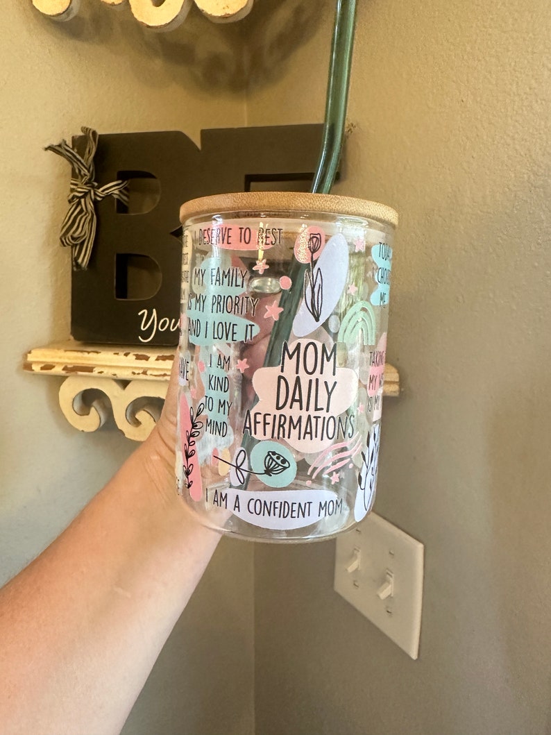 May include: A clear glass tumbler with a bamboo lid and a pink, blue, and green design. The tumbler has the text "Mom Daily Affirmations" and "I am a confident mom" printed on it.