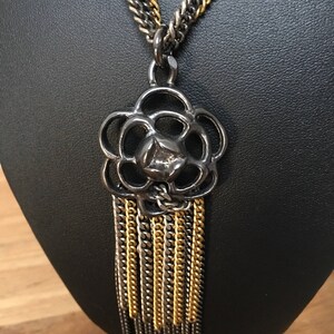 Peut inclure: Un collier en chaîne argent et or avec un grand pendentif en argent orné en forme de fleur. Le pendentif a un gland de chaînes argent et or.