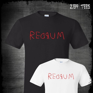 Puede incluir: Dos camisetas, una negra y una blanca, con la palabra "REDRUM" escrita en rojo en la parte delantera. La palabra está escrita en un estilo de escritura infantil y garabateado.
