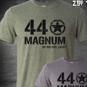 Può includere: Due t-shirt con una stampa grafica nera usurata di una stella e il testo "44 MAGNUM DO YOU FEEL LUCKY?" su una t-shirt verde e una t-shirt grigia.