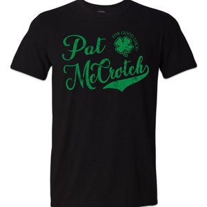 May include: Black t-shirt with green text that reads "Pat McCroch" and a green four-leaf clover with the text "For Good Luck!" above it.