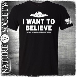 Puede incluir: Camiseta negra con la frase "I WANT TO BELIEVE" y un gráfico de OVNI blanco. También incluye la frase "BUT NOW THE GOVERNMENT SAYS THEY'RE REAL". La camiseta tiene el logo "NATURE V SOCIETY" en el lateral.
